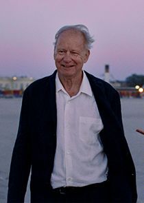 &Auml;lterer Mann steht an einem Gew&auml;sser, Wind im Haar und in der Kleidung, fr&ouml;hlich