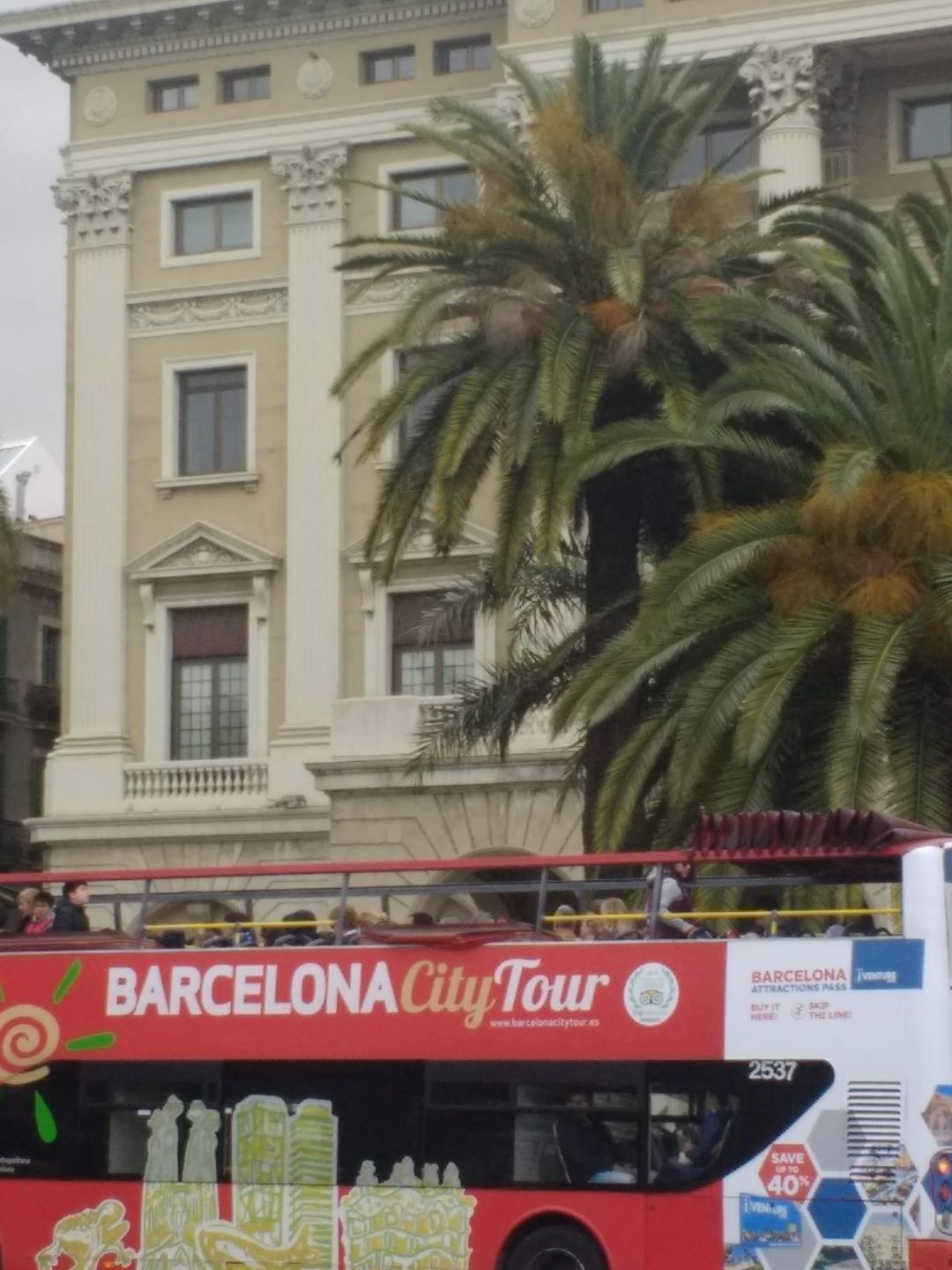roter Bus mit der Aufschrift Barcelona City Tour vor einem Geb&auml;ude mit Palmen